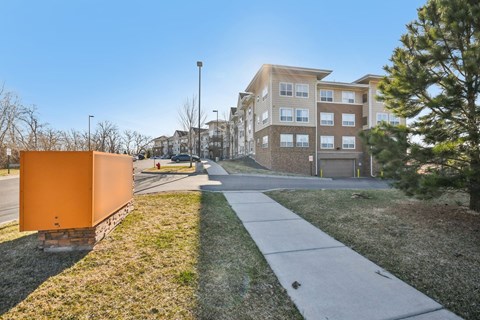 A sidewalk leads to a building with a brown and beige facade.