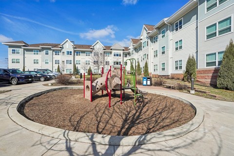 A playground with a red swing set in front of apartment buildings.