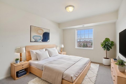 A bedroom with a large bed, a nightstand with a lamp, and a painting on the wall.