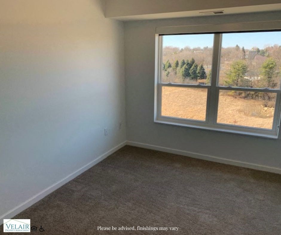 A room with a carpeted floor and a large window overlooking a field.