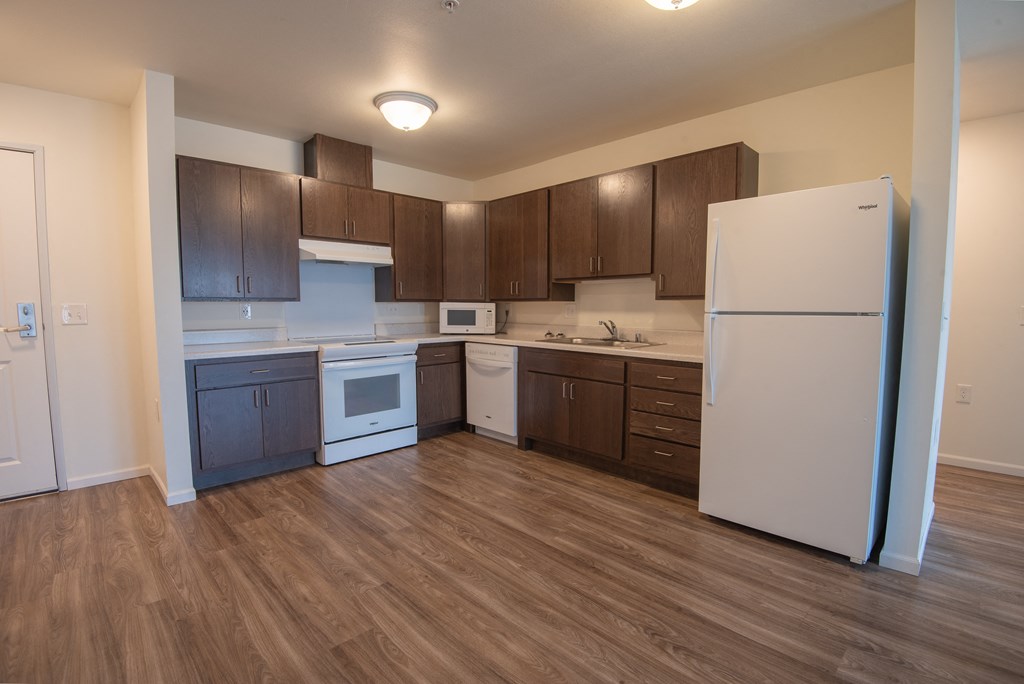 an empty kitchen with white appliances and dark wood cabinets