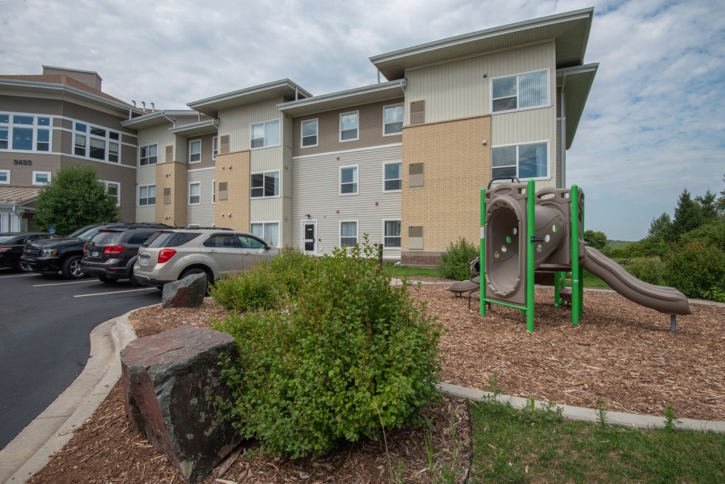 A playground with a green slide in front of a building.