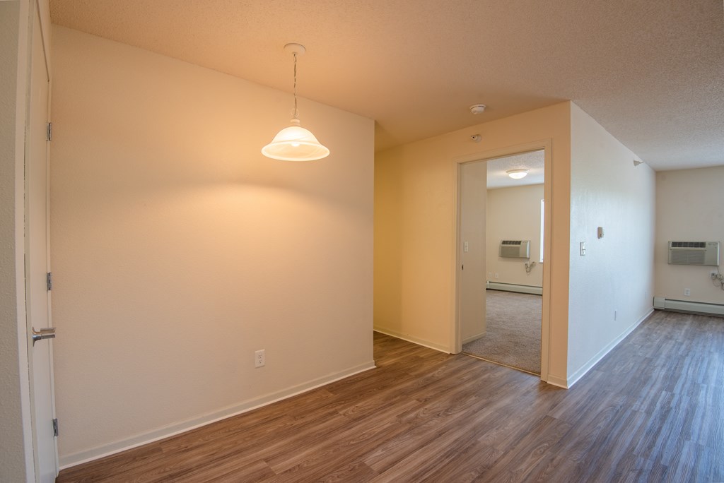 an empty living room and hallway with wood flooring and a ceiling light