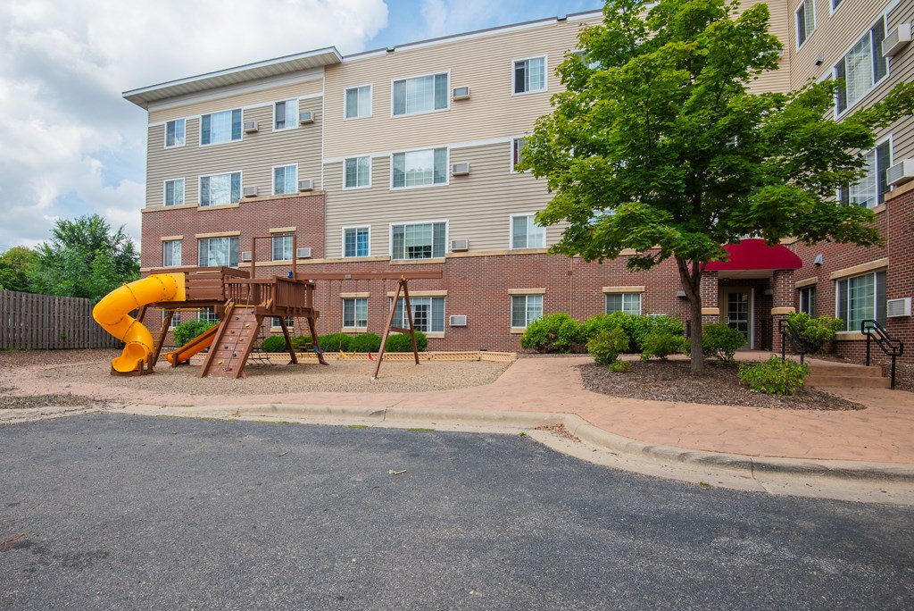 a playground in front of an apartment building with a yellow slide