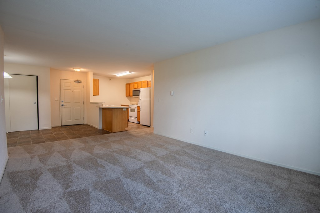 an empty living room with a kitchen in the background