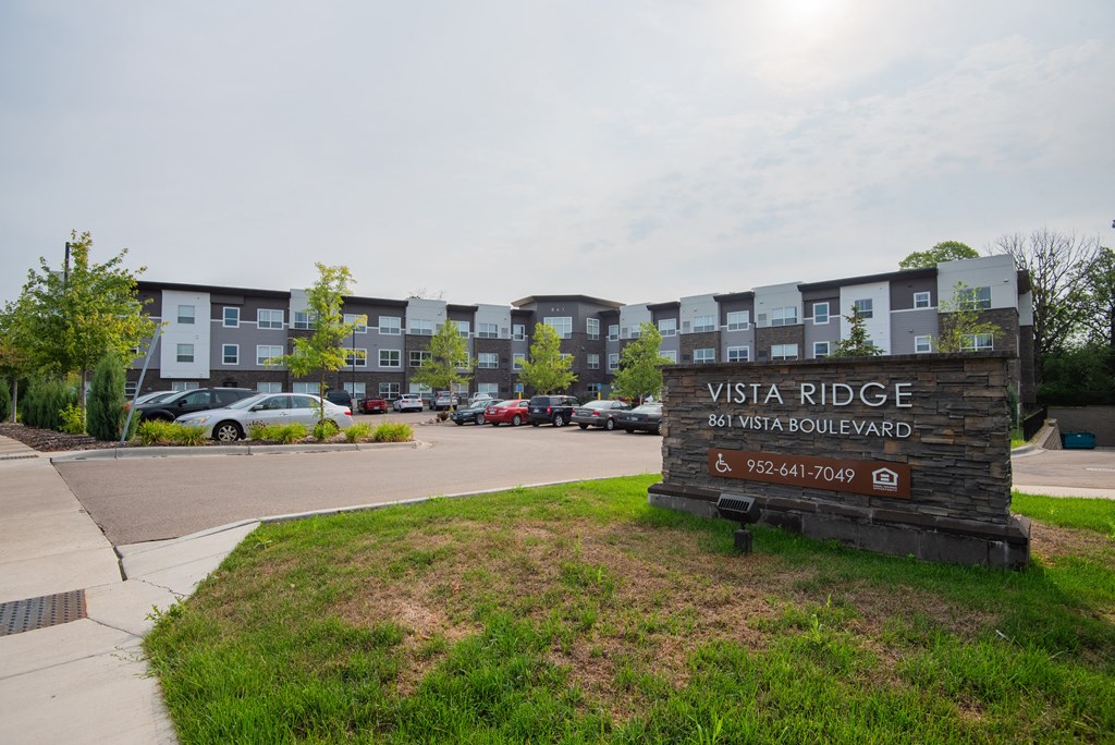 A sign for Vista Ridge stands in front of a parking lot and apartment building.