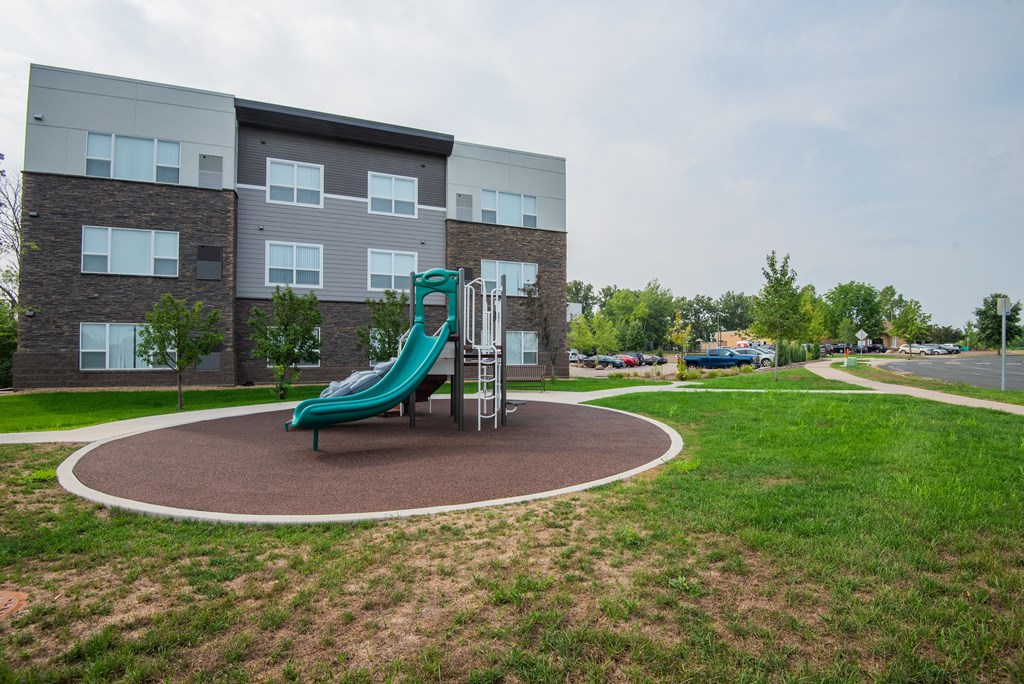 A playground with a green slide in front of a building.