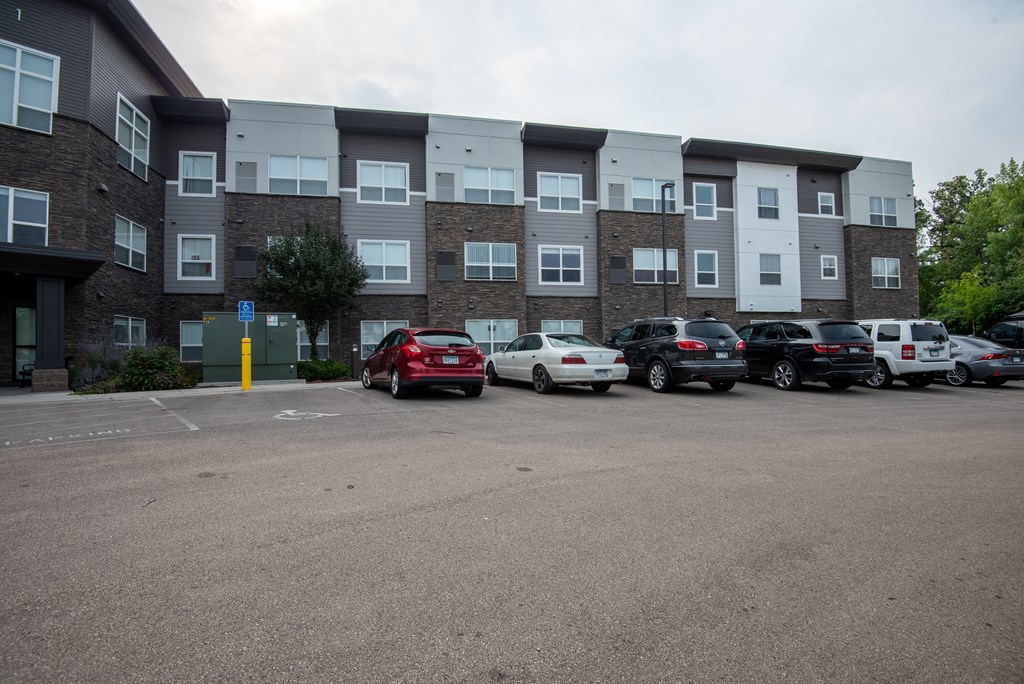 A parking lot in front of a multi-story apartment building with cars parked.