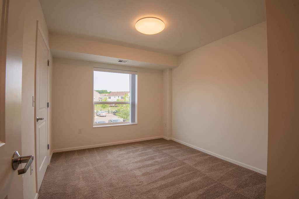 A room with a carpeted floor and a window showing a view of a house.