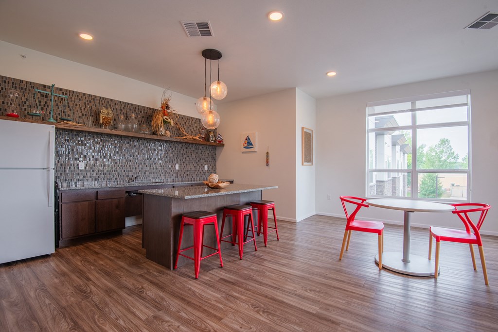 A kitchen with a white fridge, a bar area with red stools and a table with four chairs.