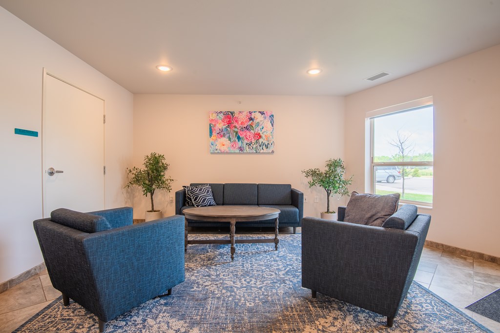 A living room with a blue rug and a painting on the wall.