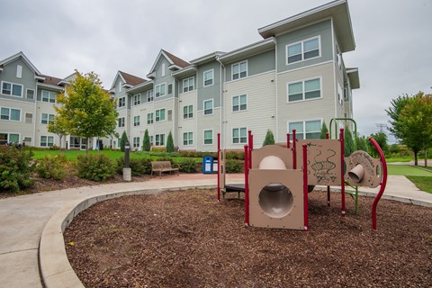 A playground with a slide and a tunnel in front of apartment buildings.