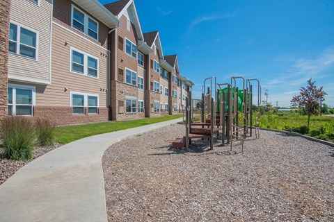 A playground with a swing set is located in front of a building with a paved walkway.