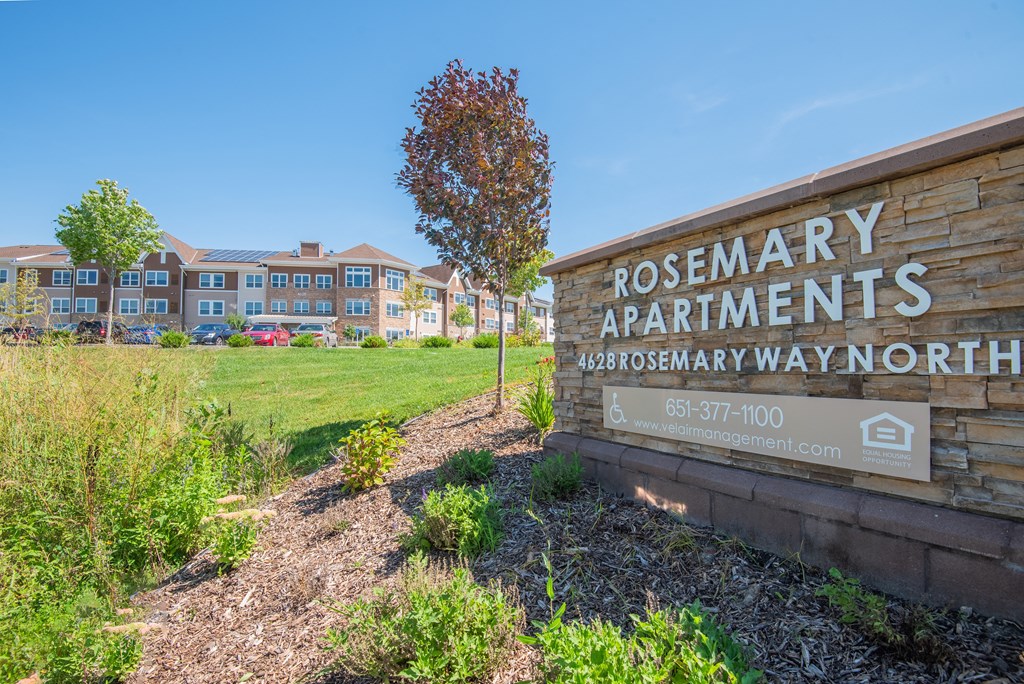 A sign for Rosemary Apartments is in front of a grassy area.