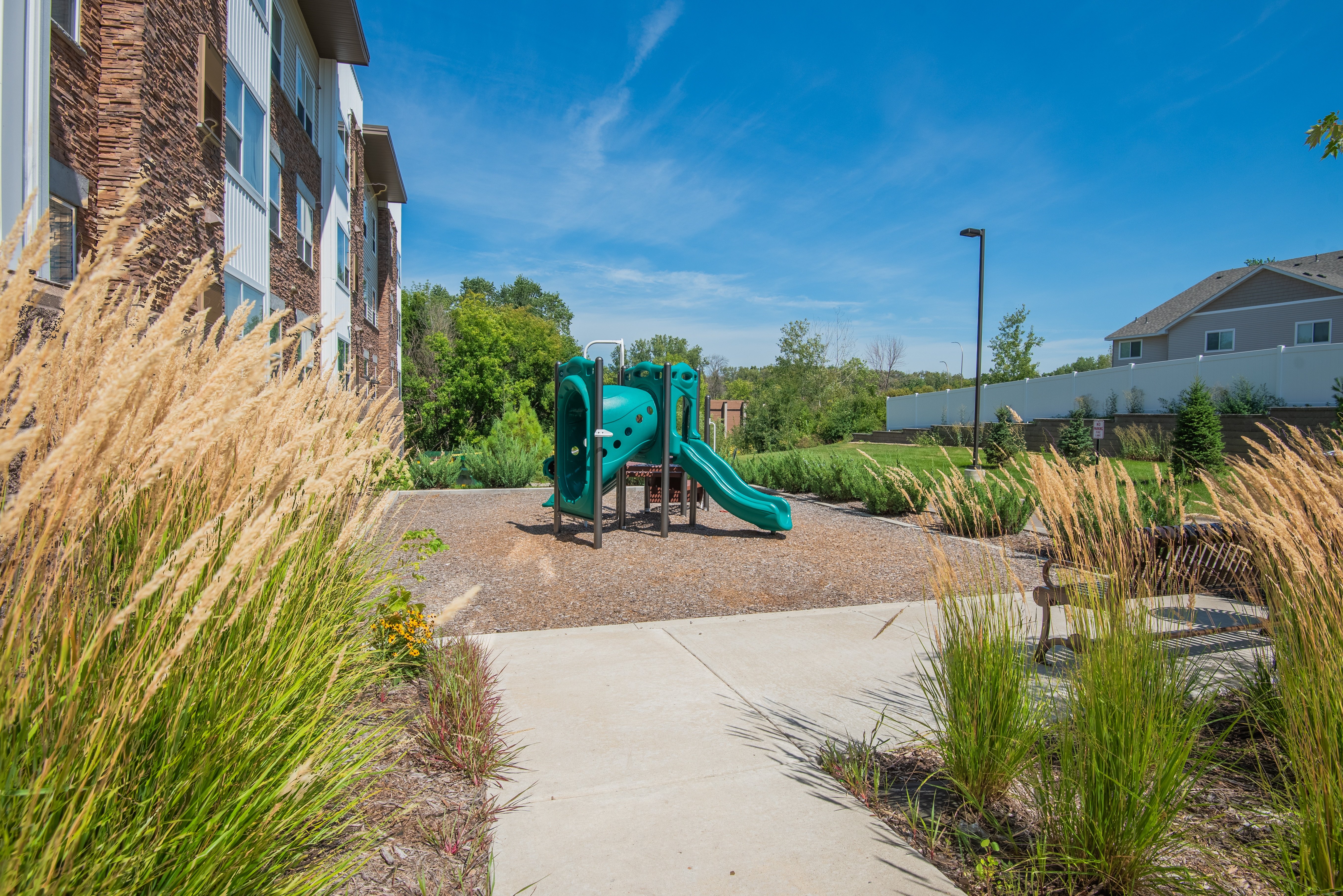 A playground with a green slide in the middle of a grassy area.