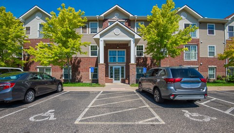 A parking lot in front of a building with cars parked and a handicap sign on the ground.