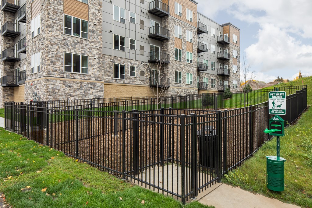 a fence in front of an apartment building with a green trash can
