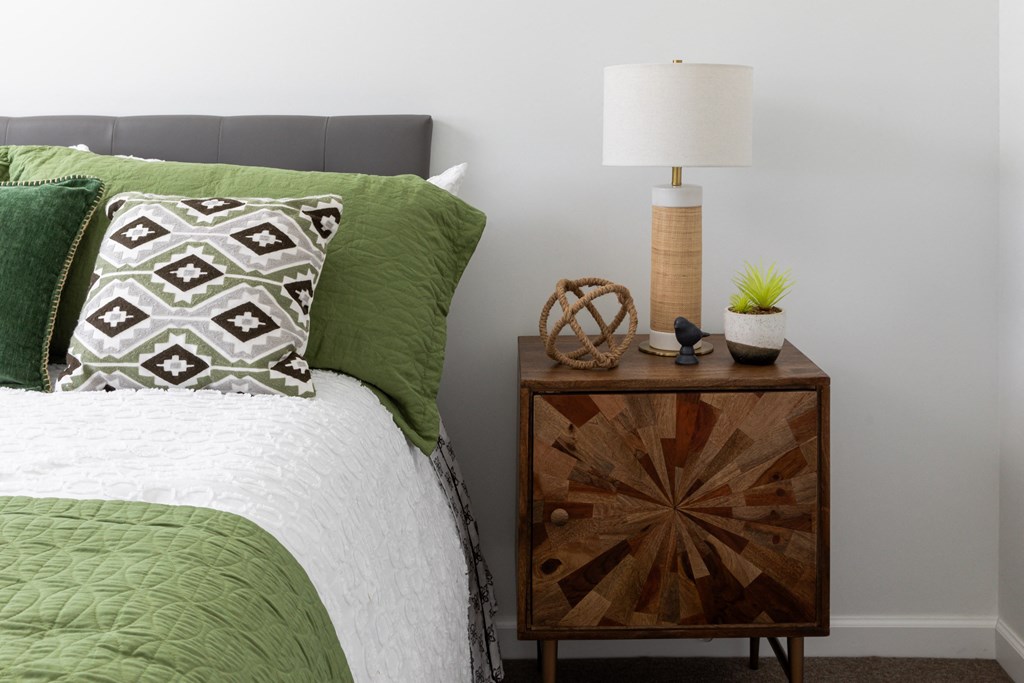 a bedroom with a bed with green pillows and a night stand with a lamp