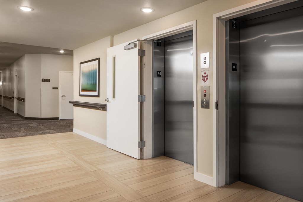 a hallway with two elevators and a wood floor and a door