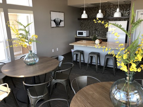 A kitchen with a table and chairs in the foreground and a microwave and fridge in the background.