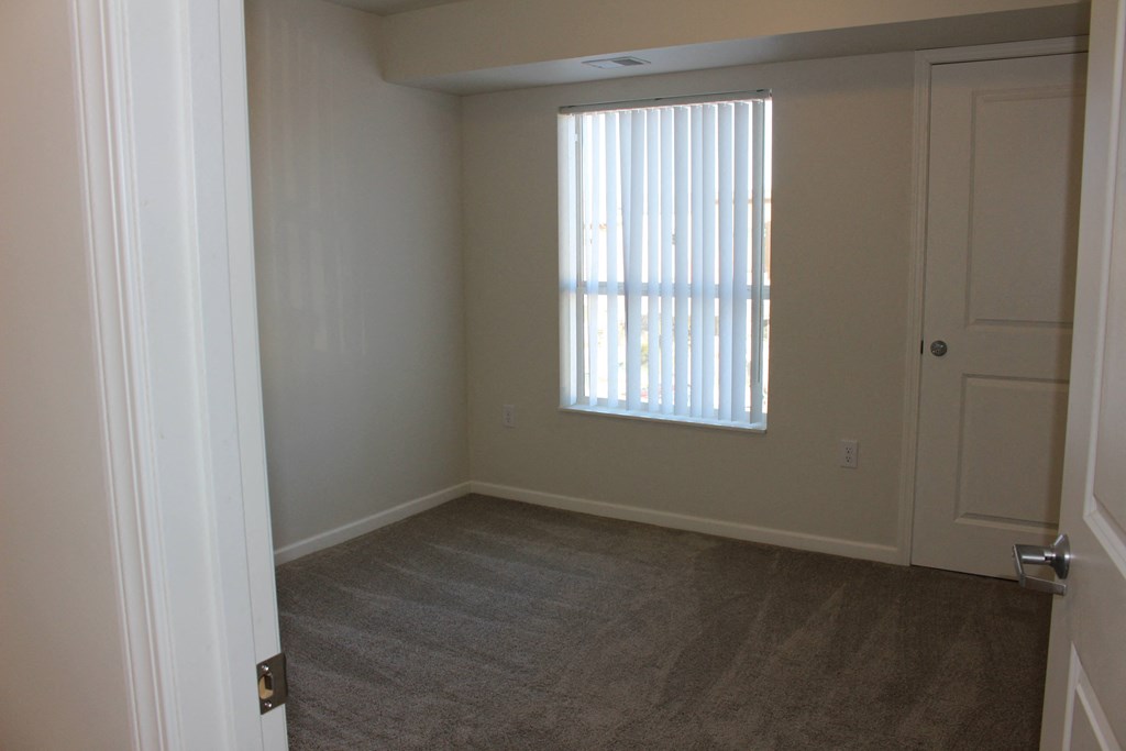 A room with a carpeted floor and a window with blinds.