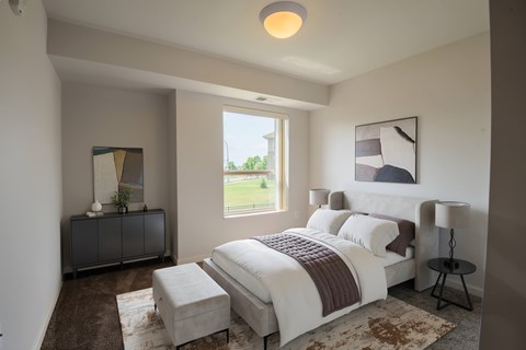 A bedroom with a large bed and a window overlooking a green lawn.