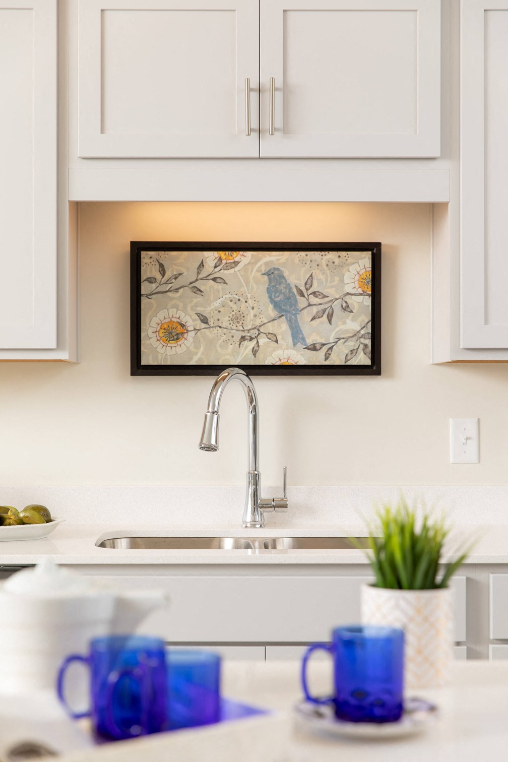 a kitchen sink with blue cups and a picture on the wall