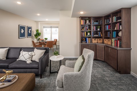 A living room with a grey sofa, a grey armchair, a coffee table, and a bookshelf filled with books.