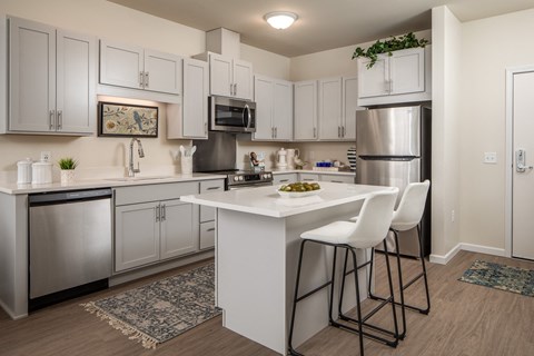 A kitchen with white cabinets and a white island with two chairs.