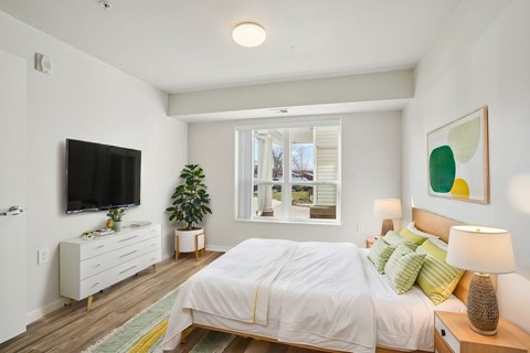 A bedroom with a large bed, a flat screen TV, and a window with blinds.