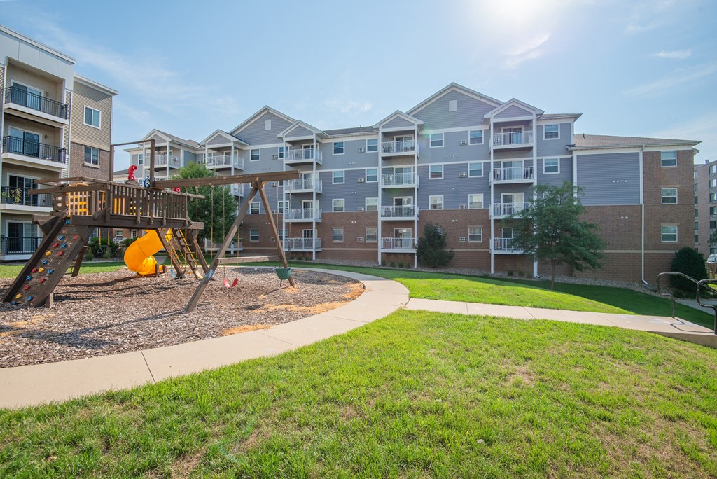 a playground with a swing set in front of an apartment building