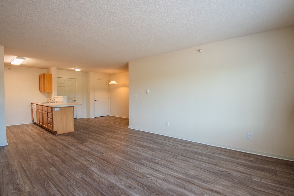 an empty living room and kitchen with wood flooring and white walls