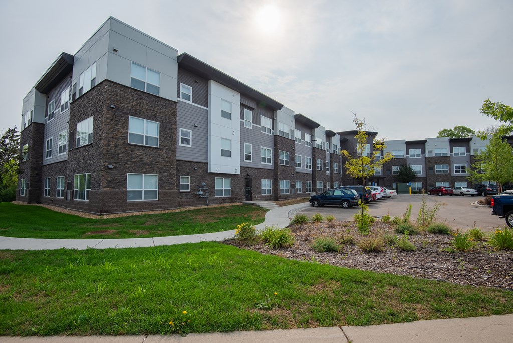 an exterior view of an apartment building with green grass and a parking lot