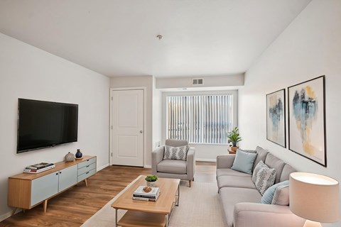 A living room with a grey couch, a wooden coffee table, and a flat screen TV mounted on the wall.