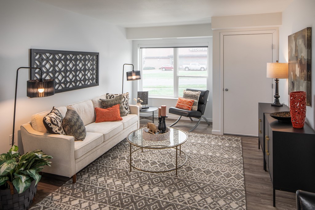 A living room with a white couch, a glass coffee table, and a large window.