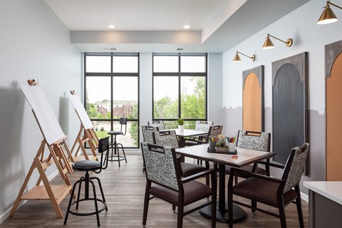 a painting studio with tables and chairs and easels and large windows
