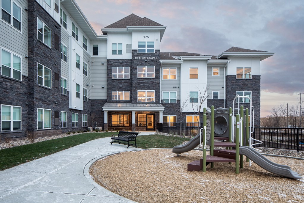 A playground with a slide and a bench in front of a multi-story residential building.