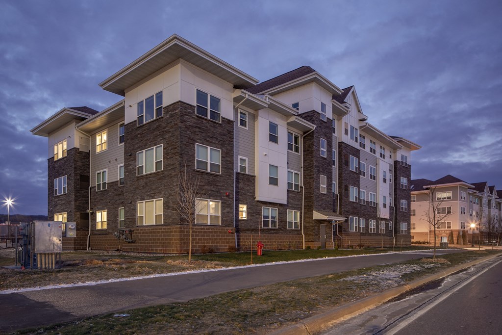 A large apartment building with multiple balconies and windows is shown at dusk.