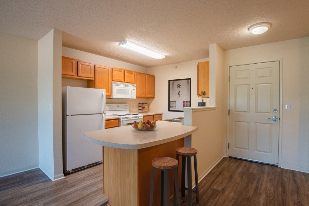 a kitchen with white appliances and wooden cabinets and a island with three stools