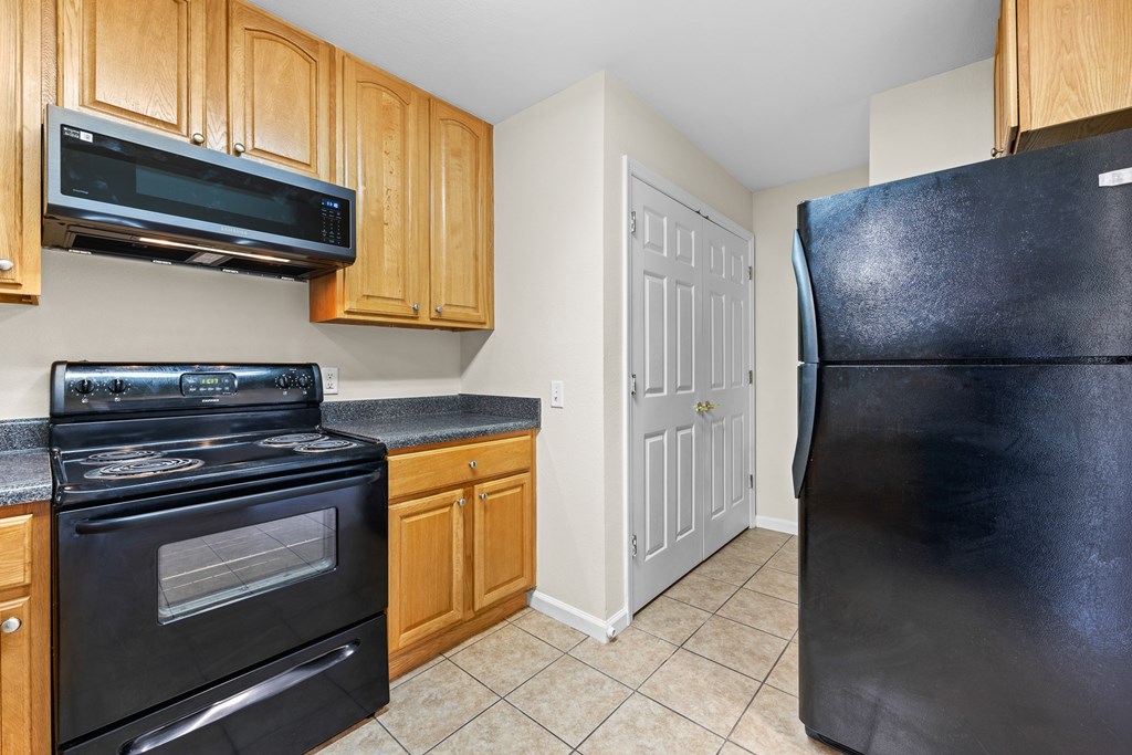 A black refrigerator stands in a kitchen with wooden cabinets and a black stove.