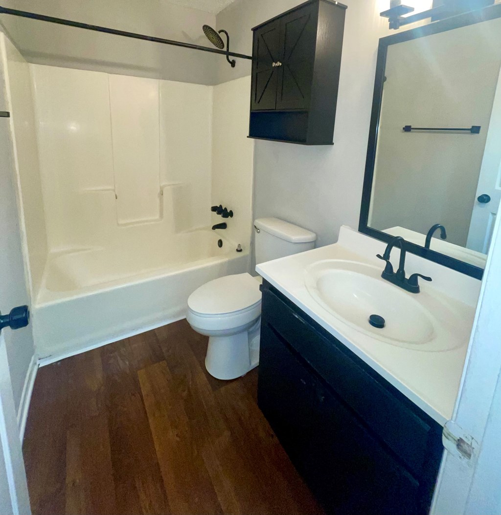 A white toilet sits in a bathroom with a black cabinet and a white sink.