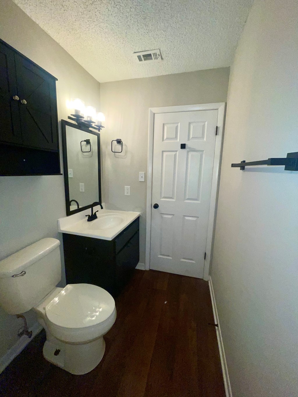 A white toilet sits in a small bathroom with a black cabinet and a white door.