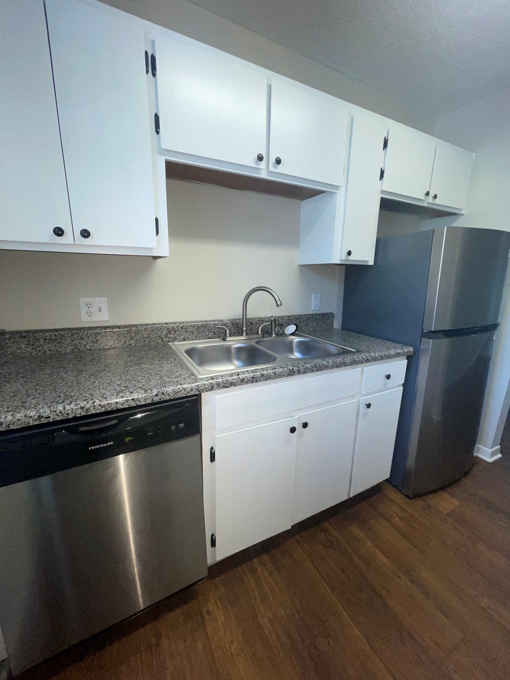 A kitchen with white cabinets and a stainless steel dishwasher and refrigerator.