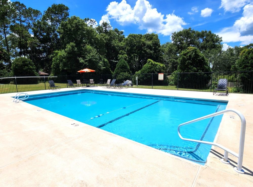 A large blue swimming pool surrounded by a fence and trees.