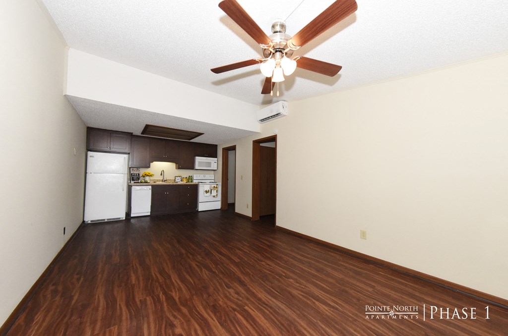 an empty living room with a ceiling fan and a kitchen