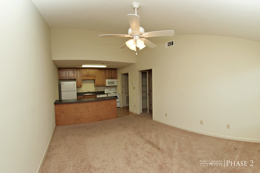 an empty living room with a ceiling fan and a kitchen