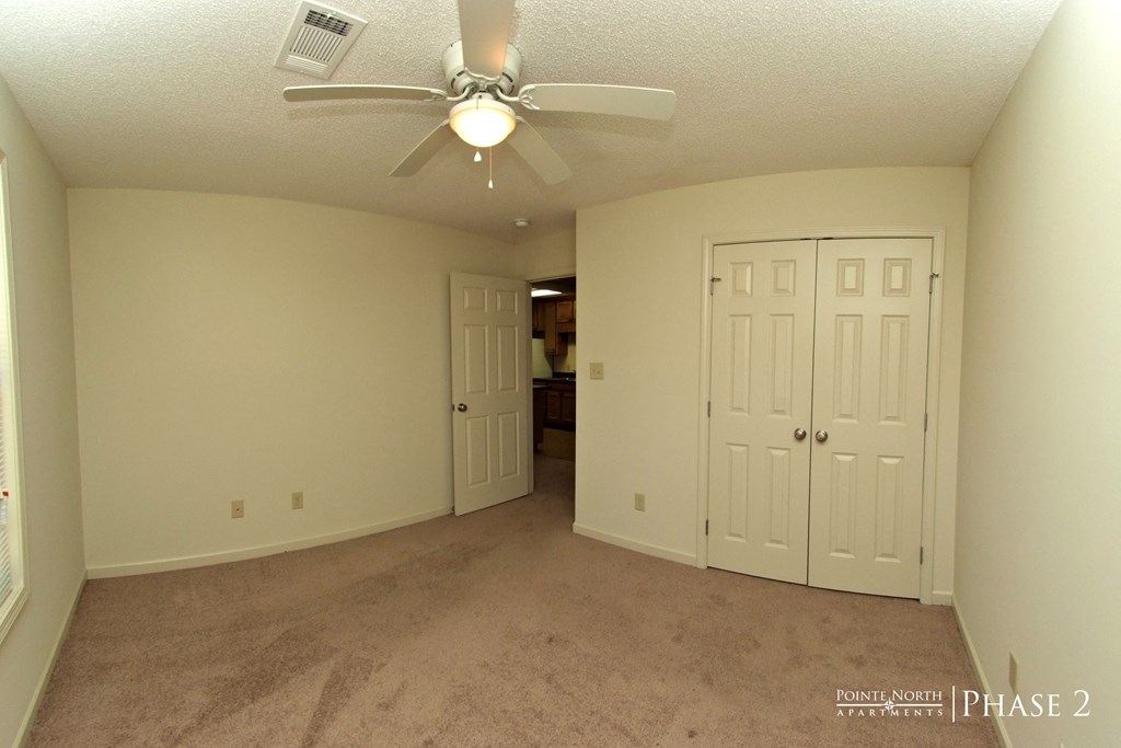 an empty living room with a ceiling fan and a closet