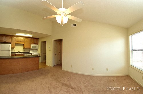 an empty living room with a ceiling fan and a kitchen