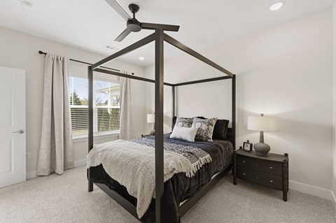 A bedroom with a four poster bed and a nightstand with a lamp.