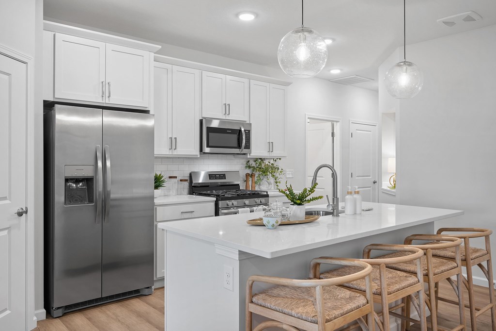 A modern kitchen with a stainless steel refrigerator, white cabinets, and wooden chairs.